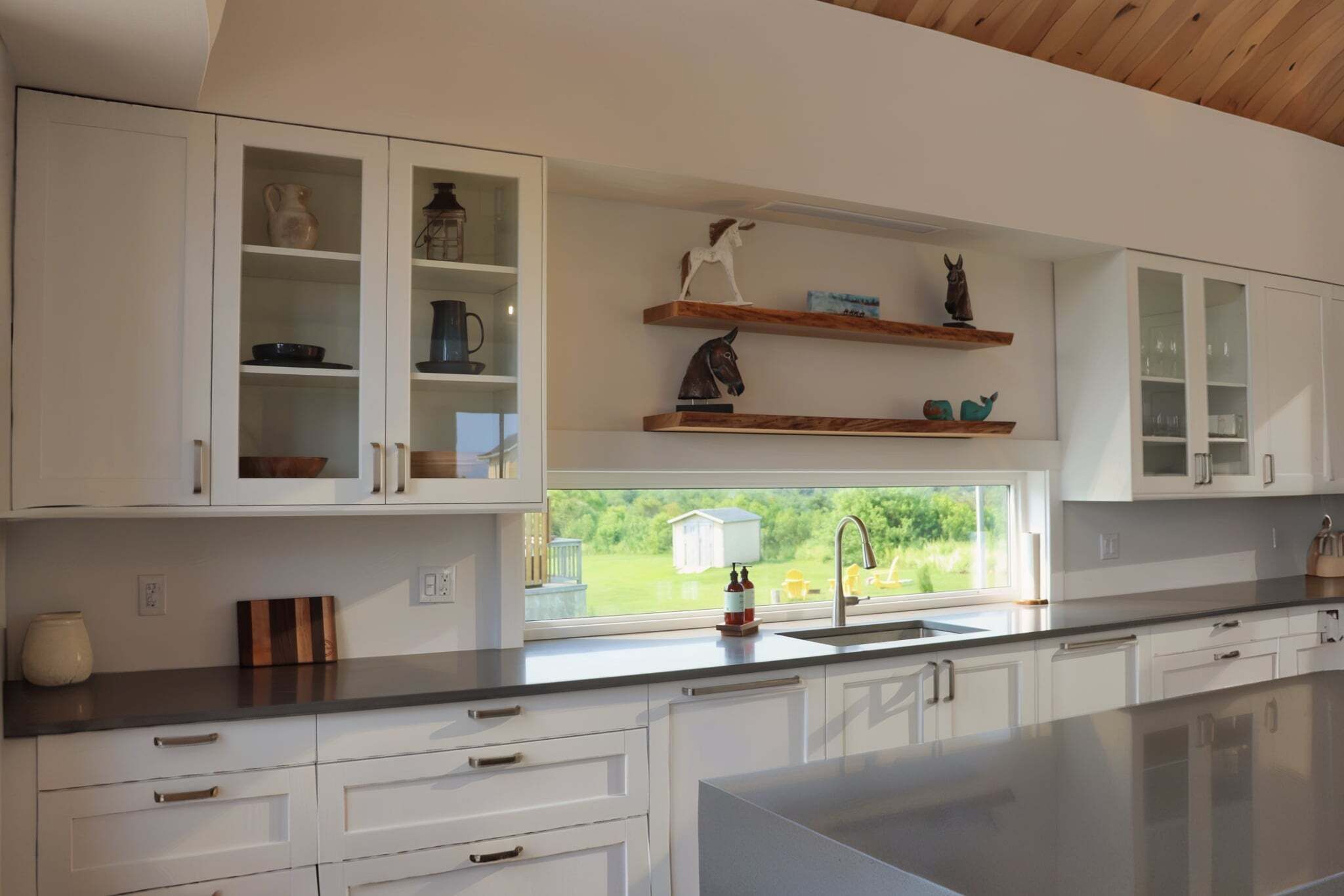 A modern kitchen with white cabinets, a large island, and a view of greenery outside.