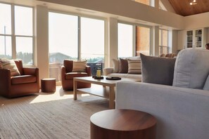 Un salón amplio con ventanas grandes, un sofá, sillones y una mesa de centro.