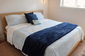 A bed with a wooden headboard, striped bedding, and a blue blanket. - Modern Beach House with Beach Access (Sea View Center)
