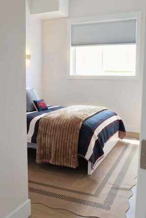 A bedroom with a bed, a window with blinds, a rug, and a wall-mounted light. - Modern Beach House with Beach Access (Sea View Center)