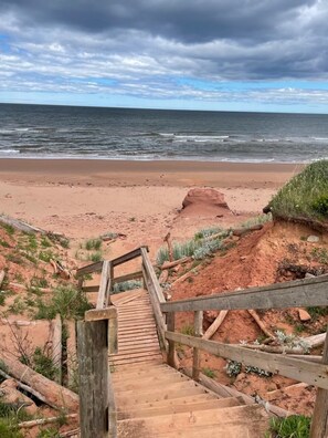 A wooden staircase leading to a beach with a view of the ocean and cloudy sky. - Modern Beach House with Beach Access (Sea View Center)