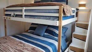 Een stapelbed met gestreepte lakens, een nachtkastje en een wandlamp.