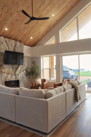 Een moderne woonkamer met een modulaire bank, een accentmuur van steen, een flatscreen televisie en grote ramen met uitzicht op het landschap.