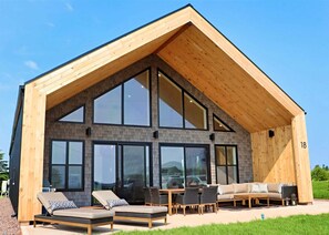 A modern house with a large wooden roof, multiple windows, and a patio with outdoor furniture. - Modern Beach House with Beach Access (Sea View Center)
