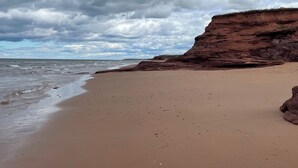 Een strand met een rotsklif en een bewolkte lucht.