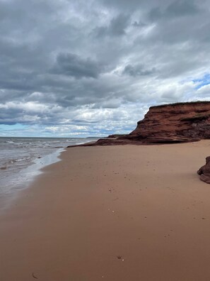 A beach with a rocky cliff and a cloudy sky. - Modern Beach House with Beach Access (Sea View Center)