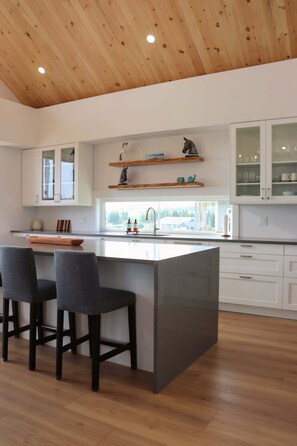 Een moderne keuken met een centraal eiland, barkrukken, houten vloeren en uitzicht door het raam.