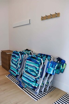 A room with a wall-mounted rack holding multiple striped bags, a wicker basket, and a white shelf. - Modern Beach House with Beach Access (Sea View Center)