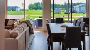 Een ruime kamer met een hoge plafond, grote ramen, een eethoek en een zithoek met een bank.