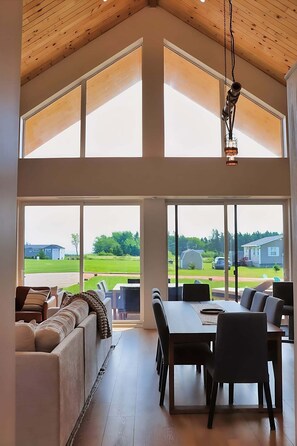 A spacious room with a high ceiling, large windows, a dining area, and a seating area with a sofa. - Modern Beach House with Beach Access (Sea View Center)
