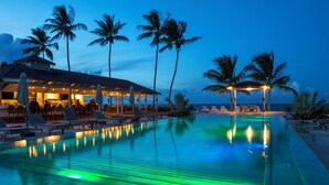 Ein Poolbereich mit Liegestühlen, einer Bar und einem Gebäude mit überdachter Terrasse.
