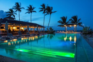 Ein Poolbereich mit Liegestühlen, einer Bar und einem Gebäude mit überdachter Terrasse.