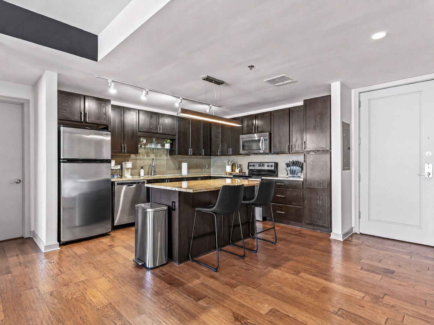 A modern kitchen with dark wood cabinets, stainless steel appliances, and a central island with bar stools.