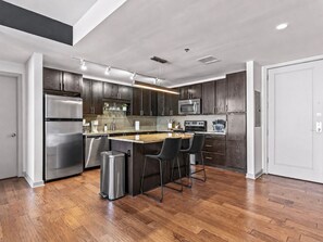 A modern kitchen with dark wood cabinets, stainless steel appliances, and a central island with bar stools. - Luxury Downtown Dallas Penthouse w/ Rooftop Pool, Gym, Free Parking (Dallas)