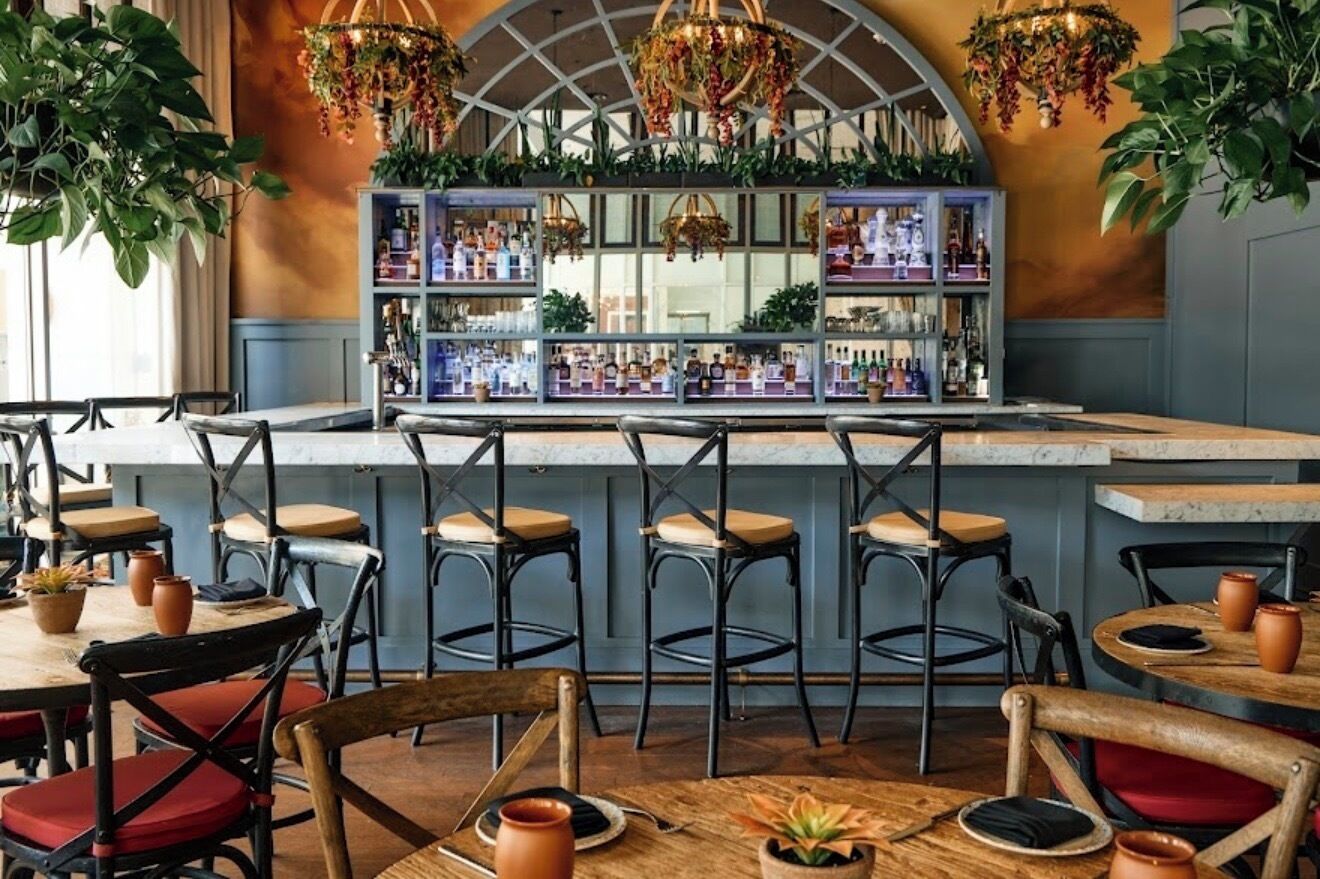 Zona de bar con taburetes, barra y estantes con botellas.