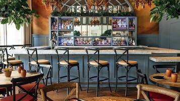 Zona de bar con taburetes, barra y estantes con botellas.