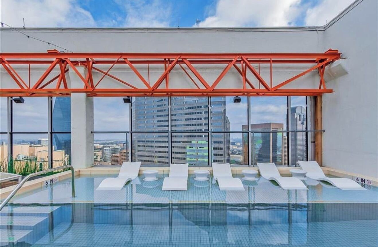 Piscina infinita en la azotea con sillones blancos y una estructura de metal rojo.