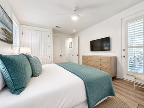 Ein Schlafzimmer mit einem Bett, einem Fernseher, einem Schminktisch und einer Tür mit Jalousien.