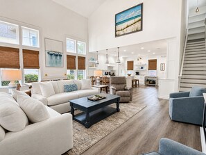 A spacious living room with a large sofa, a coffee table, and a dining area with a kitchen in the background. - 2 Golf Carts☀️ On Raven Golf Course | Heated Pool | Hot Tub | Gym | Beach Gear ☀️Sandestin (Miramar Beach)
