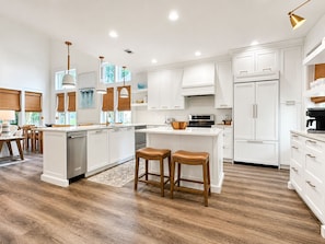 A modern kitchen with white cabinetry, a central island, wooden stools, and a stainless steel refrigerator. - 2 Golf Carts☀️ On Raven Golf Course | Heated Pool | Hot Tub | Gym | Beach Gear ☀️Sandestin (Miramar Beach)