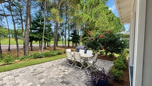 A patio with a table and chairs, surrounded by trees and a view of a road. - 2 Golf Carts☀️ On Raven Golf Course | Heated Pool | Hot Tub | Gym | Beach Gear ☀️Sandestin (Miramar Beach)
