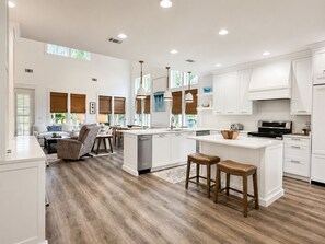 Uma cozinha espaçosa com armários brancos, uma ilha central e um espaço de refeições com sofá e cadeiras.