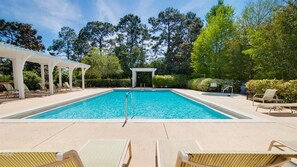 Una piscina rectangular con solárium blanco, rodeada de sillones de playa y una zona cubierta.