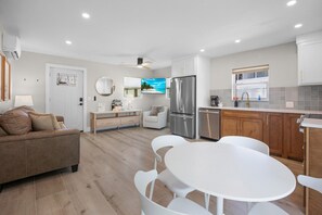 A modern kitchen with a refrigerator, stove, and dishwasher. There is a dining area with a white table and chairs. - The Eden at Coconut Cove (Fort Myers Beach)