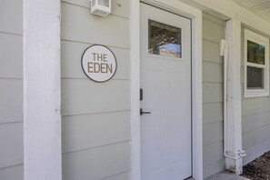 Eine weiße Tür mit einem runden Schild darüber, auf dem 'THE EDEN' steht.