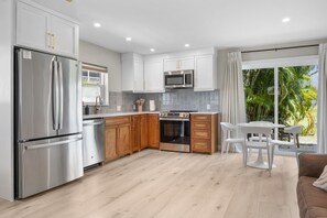 Une cuisine moderne dotée d’appareils électroménagers en acier inoxydable, de meubles en bois et d’un coin repas avec des chaises blanches.