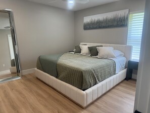 A bedroom with a bed, a bedside table, a nightstand, a window with blinds, a ceiling fan, and a wall-mounted artwork. - Delightful 3-bedroom house on the golf course (Ocala)