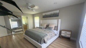 Ein modernes Schlafzimmer mit einem großen Bett, einem Nachttisch, einem Deckenventilator und einem Gemälde an der Wand.