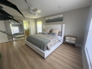 Ein modernes Schlafzimmer mit einem großen Bett, einem Nachttisch, einem Deckenventilator und einem Gemälde an der Wand.