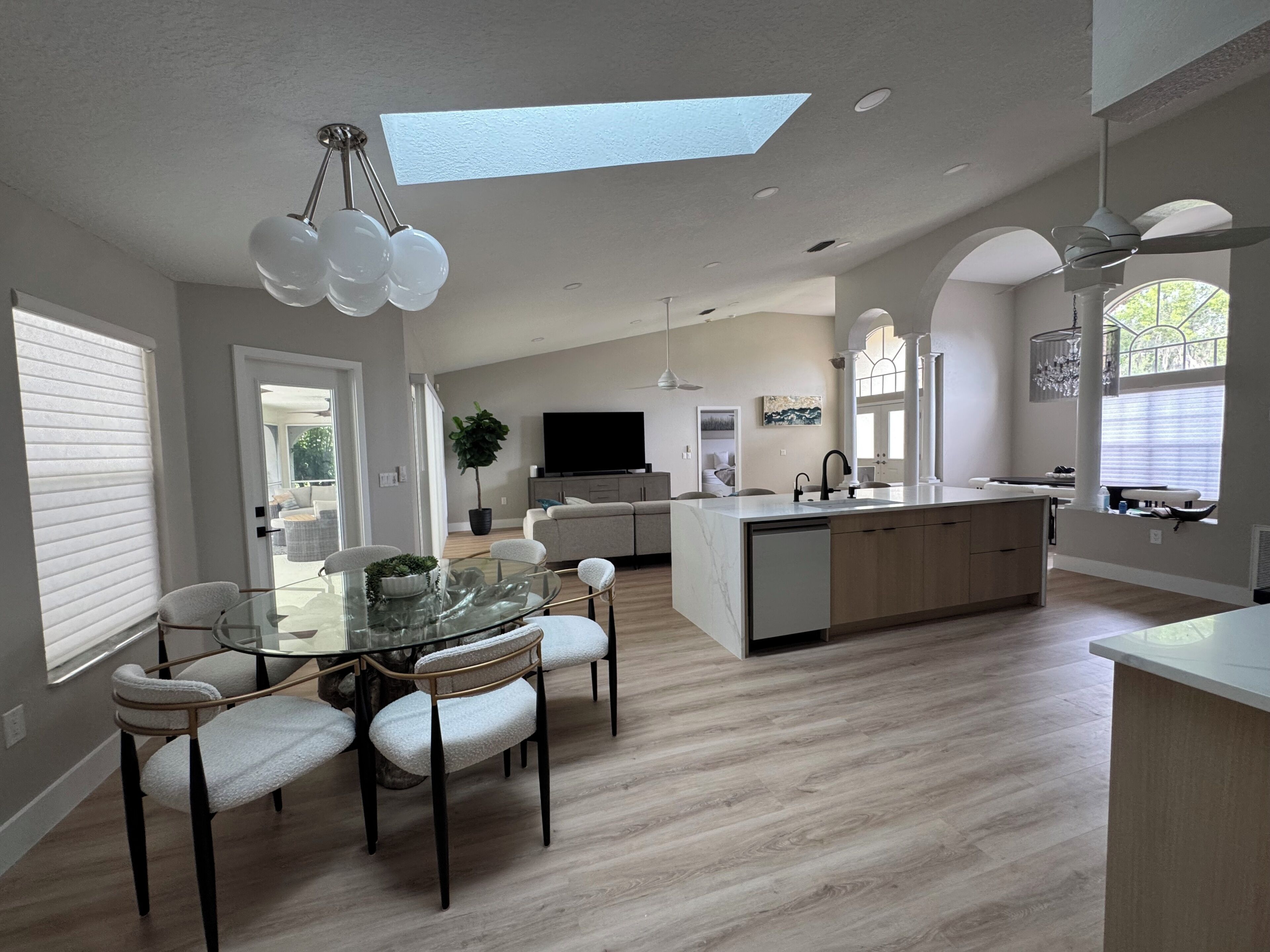 A modern kitchen with a central island, dining area with chairs, and a large window.
