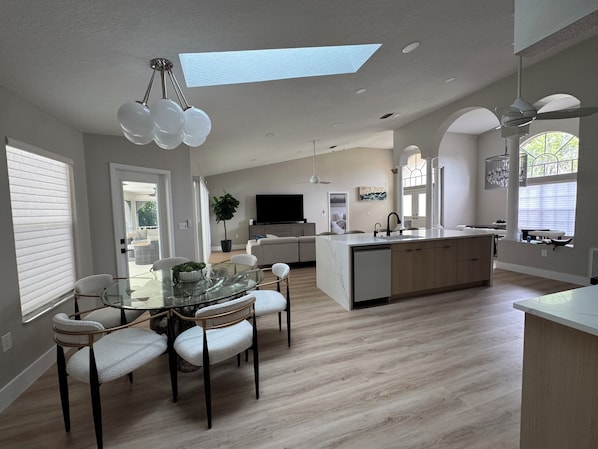A modern kitchen with a central island, dining area with chairs, and a large window.