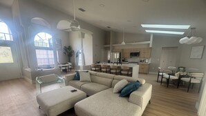 Ein geräumiges Wohnzimmer mit einem großen, beigefarbenen Ecksofa, einem Glastisch und einem Essbereich mit rundem Tisch und Stühlen.