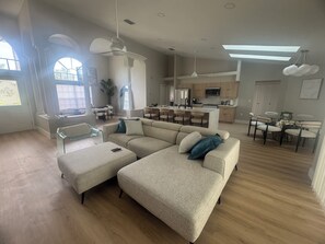 Ein geräumiges Wohnzimmer mit einem großen, beigefarbenen Ecksofa, einem Glastisch und einem Essbereich mit rundem Tisch und Stühlen.