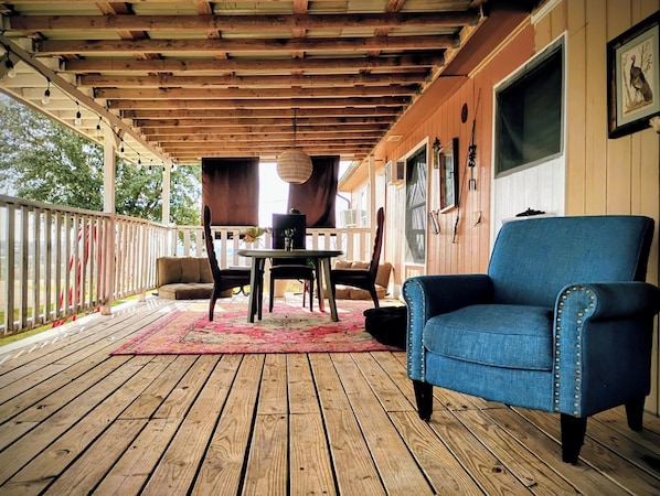 A covered porch with a wooden floor, a table with chairs, and a blue armchair.
