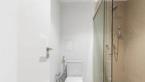 A modern bathroom with a glass shower enclosure, a toilet, and a small sink. - In Building w/ gym in Jardins Hmj0301 (São Paulo)