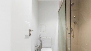 A modern bathroom with a glass shower enclosure, a toilet, and a small sink. - Studio in Building w/ gym in Jardins Hmj0301 (São Paulo)