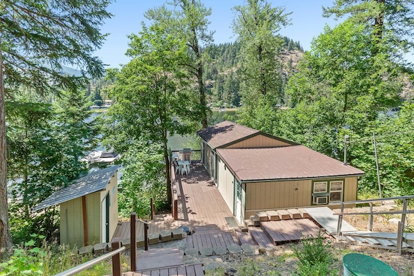 A cabin with a deck, surrounded by trees and a lake view.