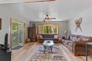 A living room with a sofa, a coffee table, a television, and a ceiling fan.