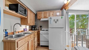 Cocina compacta con armarios de madera, microondas integrado, refrigerador blanco y estufa.