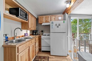 A compact kitchen with wooden cabinets, a built-in microwave, a white refrigerator, and a stove. - Rustic Twin Lakes Cabin | Private Dock, SUPs (Rathdrum)