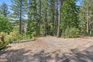 A gravel parking area with a wooden fence and a paved path leading into a forested area. - Rustic Twin Lakes Cabin | Private Dock, SUPs (Rathdrum)