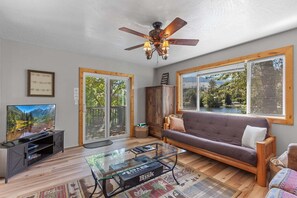 A living room with a sofa, a coffee table, a television, and a ceiling fan. - Rustic Twin Lakes Cabin | Private Dock, SUPs (Rathdrum)
