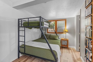 A bunk bed with a ladder, a small bedside table with a lamp, and a bookshelf with books.