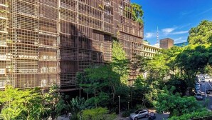 A multi-story building with a grid-like facade, surrounded by lush greenery and a street with parked cars. - Studio in Condo With Balcony in Jardins Hmj0305 (São Paulo)