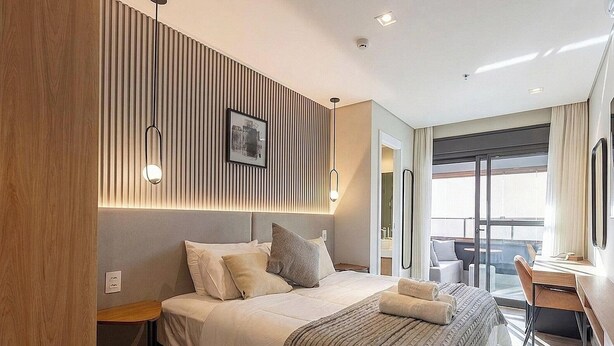 A hotel room with a bed, bedside table, and a view of the balcony. - Studio in Condo w/ Gym in Jardins Hmj0419 (São Paulo)