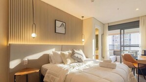 A hotel room with a bed, bedside tables, a desk, and a view of the city. - Studio in Condo w/ Balcony in Jardins Hmj0309 (São Paulo)
